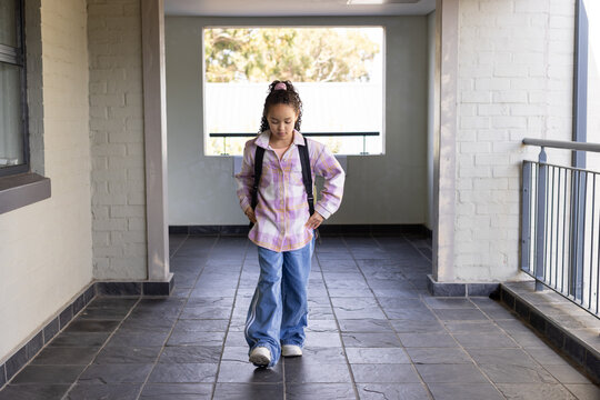 Teenage female walking down hallway at school wearing backpack plaid shirt baggy jeans sneakers
