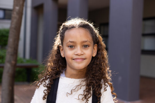 African American female child standing in courtyard by columns wearing light sweater with backpack