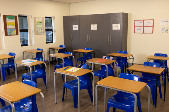Single-student desks are sitting in staggered rows in classroom, with blue chairs and folders