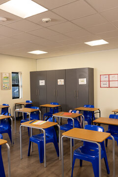 Student desks and bright blue chairs are filling classroom in staggered rows, labeled cabinets