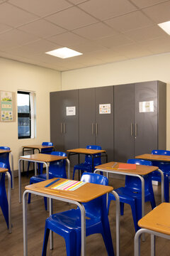 Front desk with blue chair sitting near window in classroom, holding striped folder and pencil