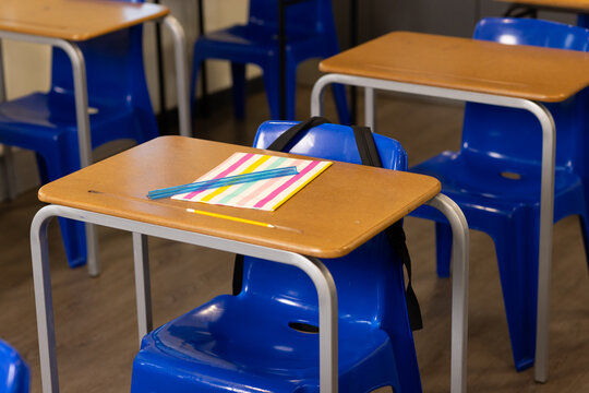 Front desk and blue chair sitting in classroom holding striped notebook, pencil, backpack hanging