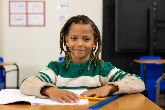 African American boy sitting at desk in classroom, hands on workbook with yellow pencil, blue ruler