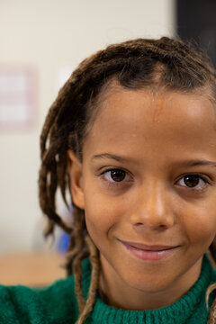 African American child smiling at camera in classroom with blurred poster, in green sweater