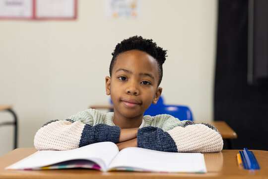 African youth male student sitting at school desk, resting forearms, wearing knit sweater, notebook