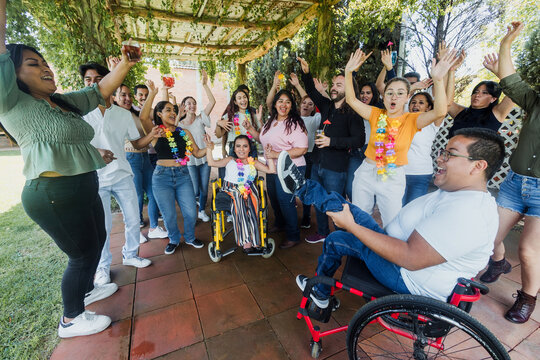 latin people in wheelchair with disabilities having fun and dancing surrounded of group of hispanic friends in party outdoors in terrace in Mexico Latin America in social inclusion concept