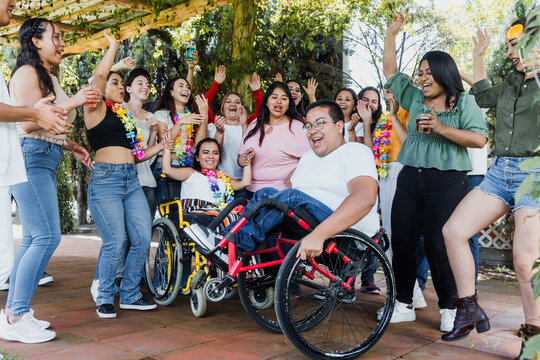 latin people in wheelchair with disabilities having fun and dancing surrounded of group of hispanic friends in party outdoors in terrace in Mexico Latin America in social inclusion concept