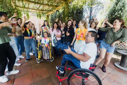 latin people in wheelchair with disabilities having fun and dancing surrounded of group of hispanic friends in party outdoors in terrace in Mexico Latin America in social inclusion concept