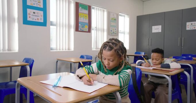 African American boys writing in notebook, front boy noticing camera, smiling holding yellow pencil
