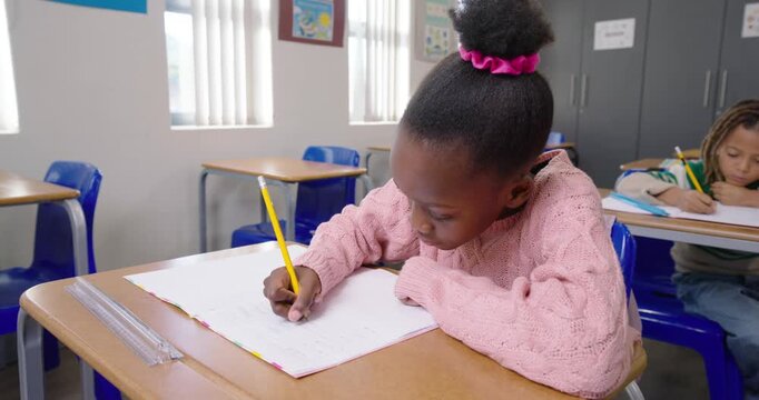 Classmates African girl child starting after prompt writing at desk with yellow pencil and notebook
