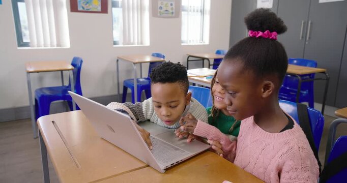 African American kids leaning in to silver laptop, taking turns tapping keys for classwork in class