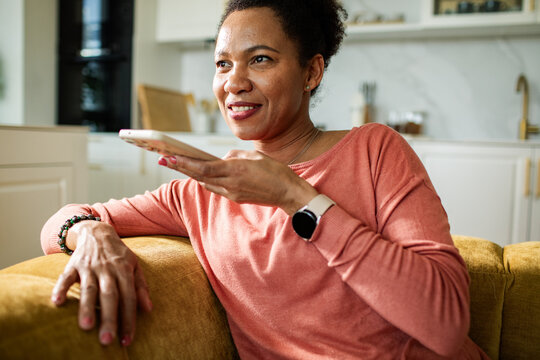 Smiling woman using voice assistant on smartphone at home