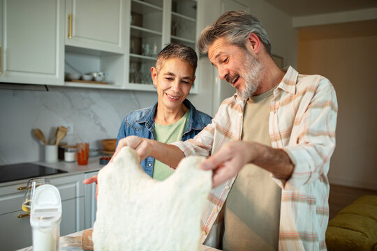 Senior couple stretching pizza dough at home kitchen