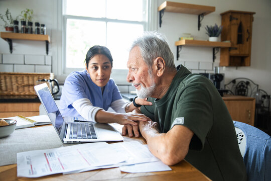 Caregiver helps senior patient review bills on laptop at home