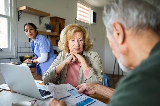 Senior couple reviewing medical bills at home with caregiver