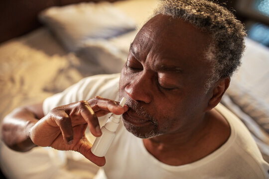 Senior man using nasal spray at home in bedroom