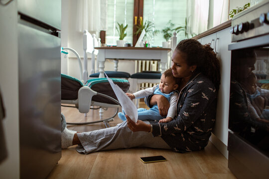 Mother reading bills with baby in kitchen