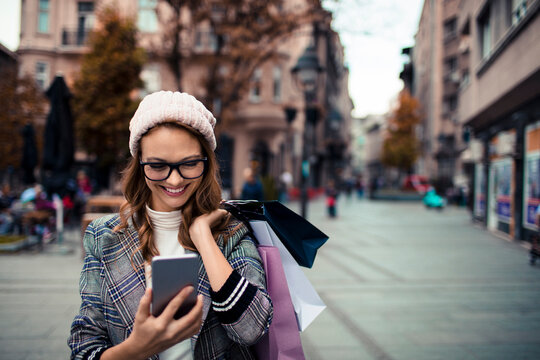 Smiling woman with shopping bags using smartphone on city street