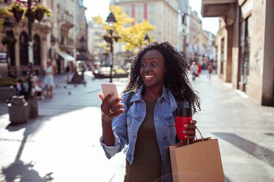Smiling young woman shopping with smartphone on city street