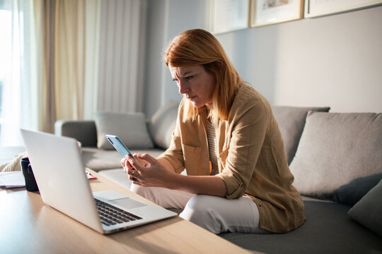 Concerned woman checking smartphone while working from home