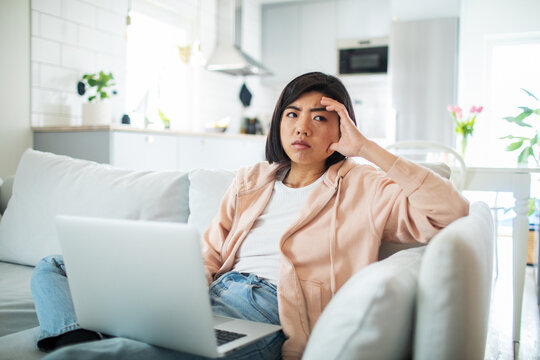 Thoughtful woman with laptop on sofa at home