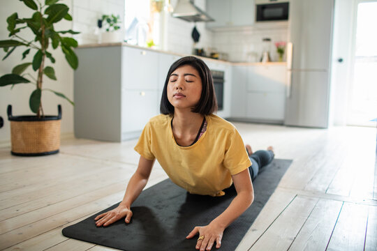 Woman practicing cobra yoga pose at home in kitchen
