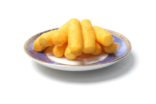 side-angle shot of a small plate filled with stacked yellow corn puff snacks against a clean white background.