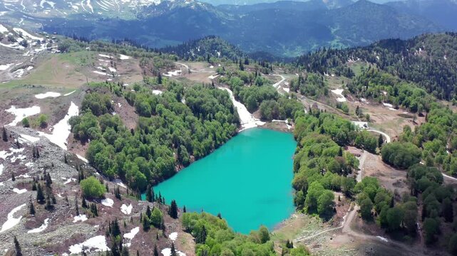 Remote Green Lake centers aerial view among woodland, alpine meadows and snow remnants in Khulo, Georgia, supporting eco-travel, hiking routes, scenic tourism and highland destination marketing.