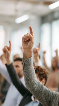 Raised hands in a group setting showing active participation and engagement. People are involved in a discussion or voting process in a bright, modern environment