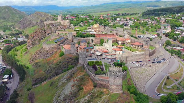 Aerial drone circles around Rabati Fortress in Akhaltsikhe, Georgia, revealing fortified walls, towers, city streets and mountain terrain heritage tourism, cultural travel and destination promotion.