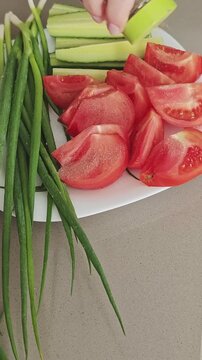 Person's hand seasoning a fresh vegetable platter with pepper. Sliced tomatoes, cucumbers, and spring onions for a healthy meal preparation