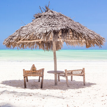 Woman reading on dack chair under wooden umbrella on white sandy tropical beach of Paje, Zanzibar, Tanzania.