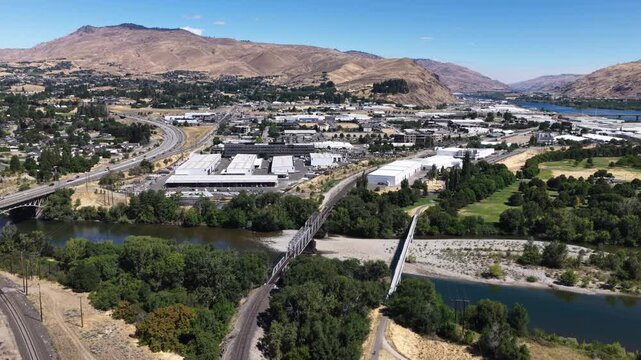 Aerial of river valley town with industrial and residential areas with wenatchee Washington showing multiple bridges crossing a river major highways train tracks