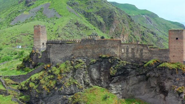 Khertvisi Fortress approaches in aerial view along a rocky cliff above green Meskheti slopes, supporting medieval history, Georgian heritage tourism, fortification studies, southern travel promotion.