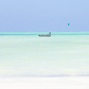 Solitary fishing boat and a kite surfer on picture perfect white sandy beach with turquoise blue sea, Paje, Zanzibar, Tanzania. Copy space.
