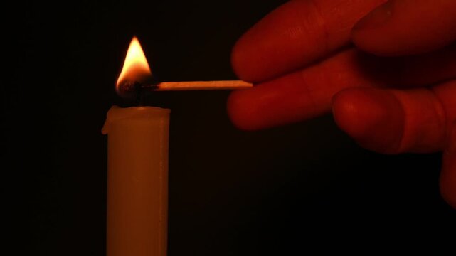 hand bringing a burning match to a candle wick in close up view