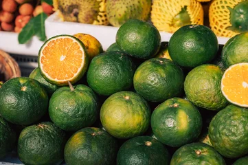 Close-up of green oranges with sliced fruit at a market, showcasing fresh citrus produce and vibrant natural colors. © olinchuk