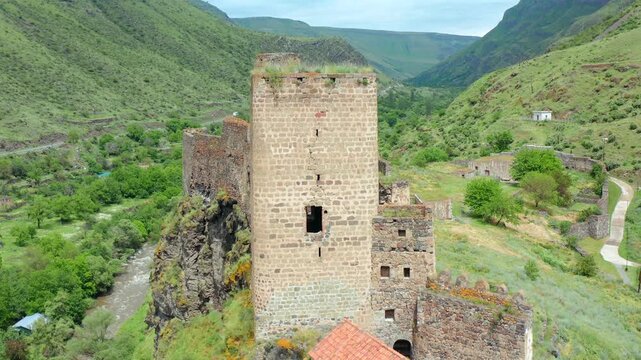 Khertvisi tower rises, elevated aerial view above fortified walls and green mountain slopes, supporting medieval architecture, monument conservation, Georgian tourism and history media production.