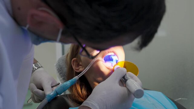 Pediatric dentist using UV curing light lamp on tooth filling for young girl.