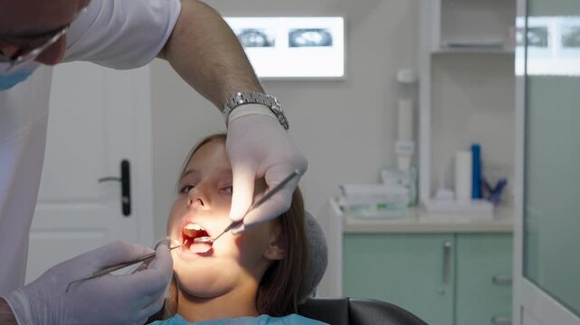 Pediatric dentist polishing tooth filling with handpiece for young girl close up