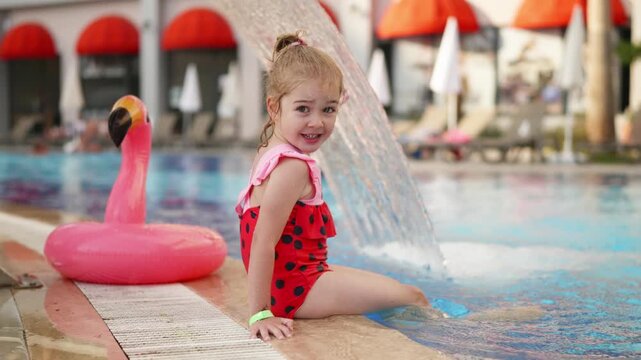 Child enjoys splashing water by the poolside with a flamingo float in warm sunny weather