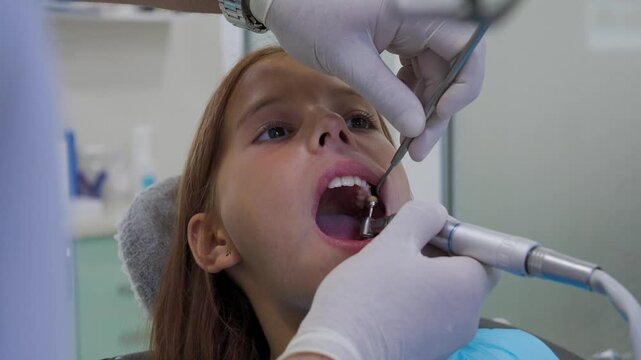 Pediatric dentist polishing tooth filling with handpiece for young girl close up