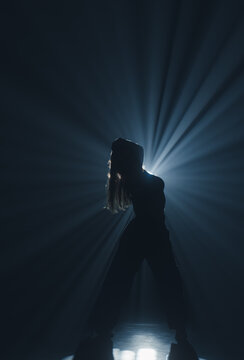 Mysterious silhouette of a female dancer under a blue spotlight beam. Concept of commercial template with copy space for musical show promo, theater poster and mental health therapy.