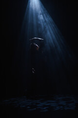 Obraz premium Mysterious silhouette of a female dancer under a blue spotlight beam. Concept of commercial template with copy space for musical show promo, theater poster and mental health therapy.