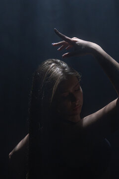 Close up of a female dancer posing with raised arm under dramatic overhead light. Concept of moody portrait for music album cover, theater poster and creative advertising.