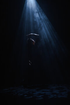 Mysterious silhouette of a female dancer under a blue spotlight beam. Concept of commercial template with copy space for musical show promo, theater poster and mental health therapy.