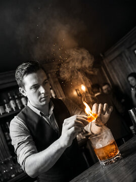 Professional bartender flaming orange peel over whiskey cocktail glass