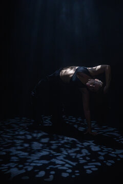 Attractive female dancer posing on floor under bright blue spotlight. Concept of expressive artistic layout for music album cover, theater poster and modern dancing class promotion.