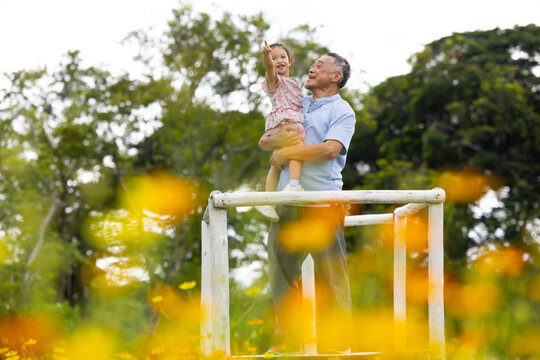 Cheerful girl and grandfather standing together on picnic and garden flowers background. Silly Family group photo. Grandfather takes pictures of child and mother father in park summer
