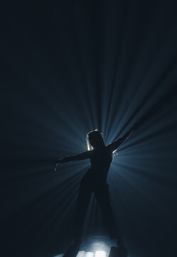 Mysterious silhouette of a female dancer under a blue spotlight beam. Concept of commercial template with copy space for musical show promo, theater poster and mental health therapy.